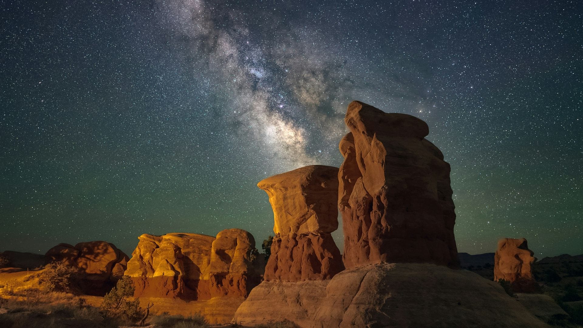 Milky Way core rising above warm-lit red sandstone hoodoos near Kanab, Utah